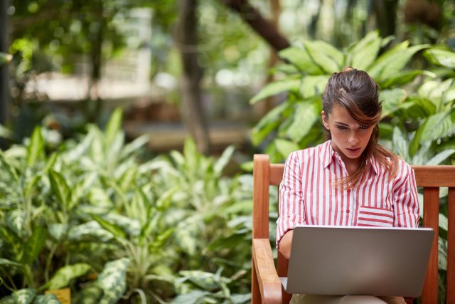 Woman reading email newsletter on laptop while sitting outside in garden